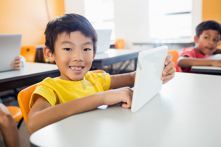 快乐的男孩在办公桌前与平板电脑合影