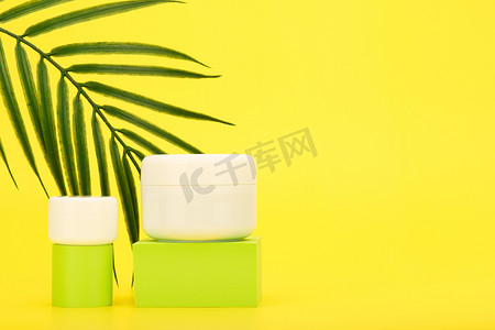 黄色背景下带棕榈叶和复制空间的绿色讲台上的奶油或面膜和润唇膏或眼霜