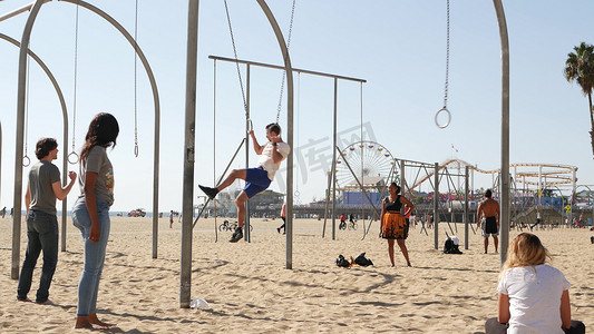 健身房运动卡摄影照片_美国加利福尼亚州洛杉矶圣塔莫尼卡 — 2019 年 10 月 28 日：加州夏季太平洋海滩美学，年轻人在运动场上训练和玩乐。