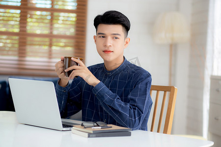 年轻商人在家工作，办公桌上放着笔记本电脑，自由职业男性坐在家里使用笔记本进行交流并在桌上放松，创业企业家，新常态。