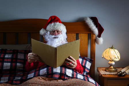 圣诞老人在平安夜睡觉前坐在床上读一本大书。