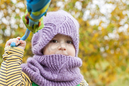 树木的孩子摄影照片_一个戴着紫色针织帽子和围巾的孩子。