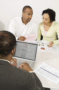 卡片文件摄影照片_一位非洲裔美国财务顾问使用笔记本电脑与夫妇在办公室讨论文件