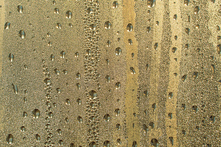 带有金色水滴的抽象背景装饰。雨滴是金色的。玻璃上闪闪发光的水面。水滴呈球形或球形。彩色雨滴