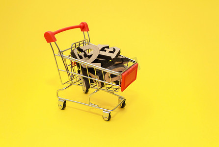 英文字母表的木制字母位于黄色背景的微型购物手推车中，特写。知识购买概念。
