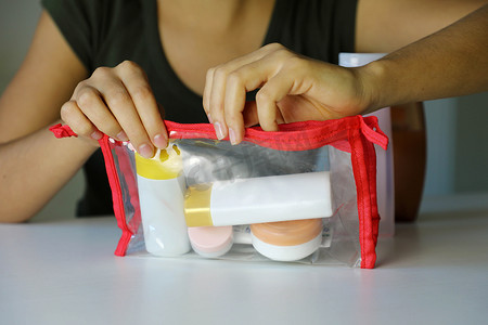 透明袋子摄影照片_女人用带旅行工具包的透明袋子在飞机上运输化妆品
