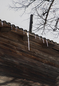 小冰柱悬挂在木屋的屋顶上，在阳光下闪闪发光。