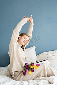 穿着睡衣坐在床上伸懒腰看书的快乐女人
