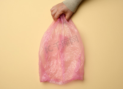 手拿着黄色背景上的空粉色塑料袋