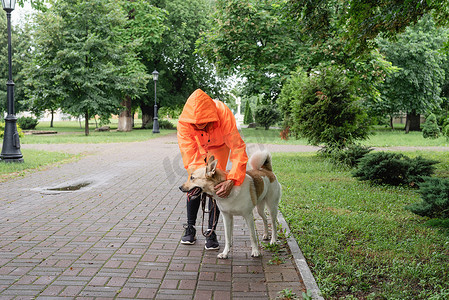 穿着橙色雨衣的年轻女子和她的狗在公园里散步