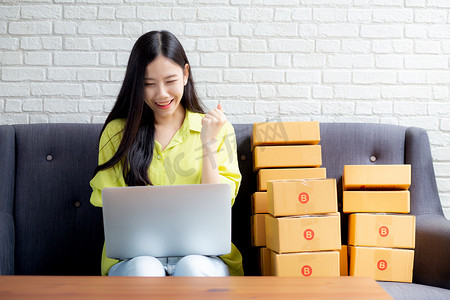 年轻的亚洲女性是商人，在沙发上使用笔记本电脑检查客户的订单，购买网上购物、商业中小企业或初创企业、企业家或卖家以及服务交付产品。