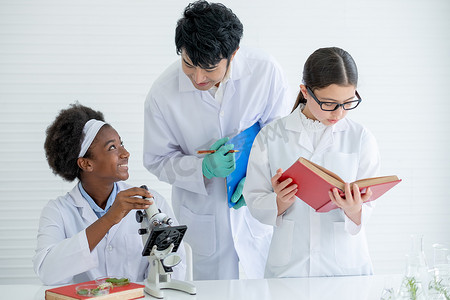 亚洲教师帮助和指导非洲裔美国年轻科学家女童在实验室或课堂上使用显微镜进行分析，而其他学生也阅读教科书。