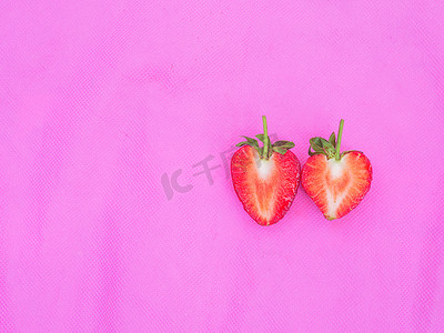 一对红心草莓甜果红色浆果心形水果的特写质地在粉红色织物背景上切成两半