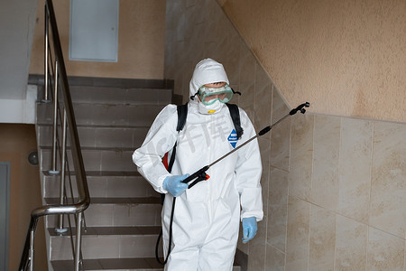 UKRAINE, KYIV - May 20, 2020：身穿白色防护服和面具的男子正在对建筑物内表面进行消毒，同时冠状病毒流行以预防感染和控制流行病。