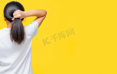 亚洲女性在黄色背景上拿着受损头发的后视图，带有复制空间。