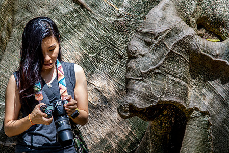 泰国乌泰他尼省 Ban Sanam 的年轻女子背着单肩包，观看相机拍摄的照片，人与巨树的大小比较。