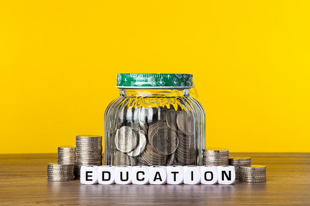 教育基金摄影照片_黄色背景玻璃瓶中的很多硬币。