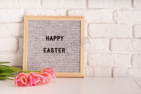 带郁金香的花瓶和灰色毡信板，白砖背景上写着复活节快乐