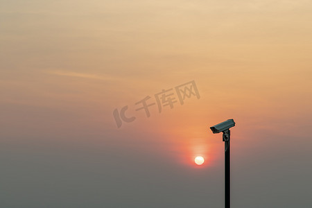 前景中的现代监控摄像机 橙色的太阳在太阳落山前闪耀。