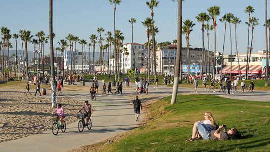 美国加利福尼亚州洛杉矶 — 2019年11月16日：加州夏季海洋威尼斯海滩美学，许多人步行和骑自行车，棕榈树间的自行车道。