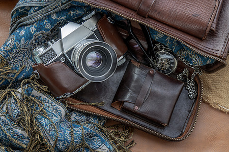 装饰怀表摄影照片_复古相机的顶部视图和带围巾、眼镜和怀表的棕色皮包在麻布背景上。