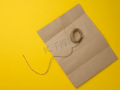 黄色背景中空白的棕色牛皮纸袋和黄麻绳
