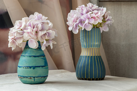 白色纹理桌布上的两个蓝色手工陶瓷花瓶中的紫色花束。
