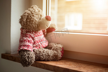 孤寂摄影照片_离开概念：泰迪熊正看着窗外，阳光