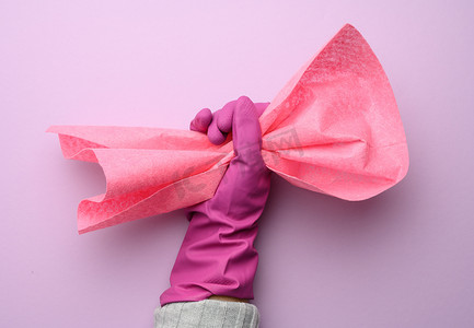 粉色橡胶手套中的女手拿着紫色背景上的粉色清洁抹布