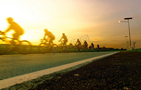 模糊的照片运动员在晚上与夕阳的天空在路上骑自行车以速度运动。