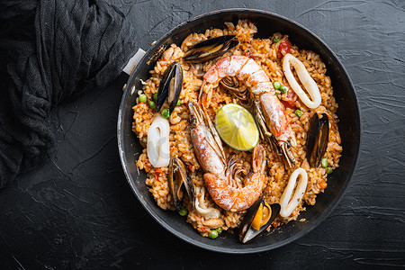 海鲜饭传统西班牙菜在煎锅中供应，黑色纹理表面，顶视图
