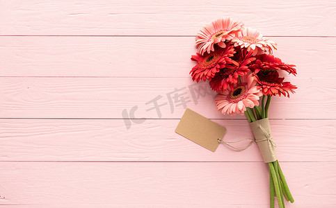粉色木桌上的红色非洲菊雏菊花和空白工艺标签