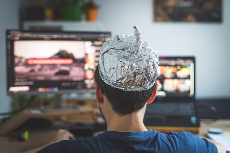 阴谋论概念：年轻人头戴铝头，坐在电脑前看视频
