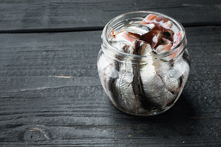 盐渍凤尾鱼片，在玻璃罐中，在黑色木桌背景上，带有复制空间和文本空间