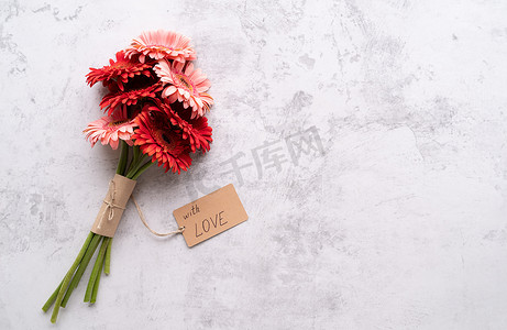 生日邀请函红色摄影照片_红色非洲菊雏菊花和工艺标签，在混凝土桌上写着“With Love”