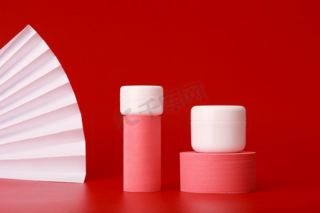 两个粉红色几何形状的奶油罐，用于在红色背景上展示带波纹的产品