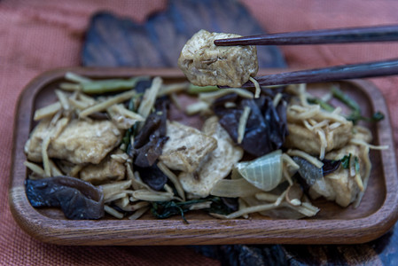 炒豆腐摄影照片_手正用筷子夹起木盘里的姜炒豆腐。