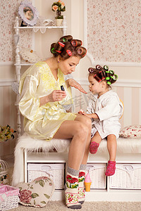 可爱的小女孩和她妈妈在卷发器上涂指甲。