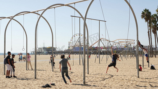 健身房运动卡摄影照片_美国加利福尼亚州洛杉矶圣塔莫尼卡 — 2019 年 10 月 28 日：加州夏季太平洋海滩美学，年轻人在运动场上训练和玩乐。