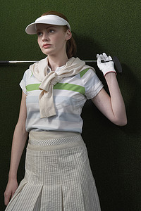 握球手摄影照片_绿色背景下肩后握着高尔夫球杆的年轻女子