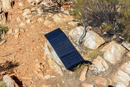 露营地岩石上的太阳能电池板为手机和相机充电，替代电源 — 可持续资源的概念