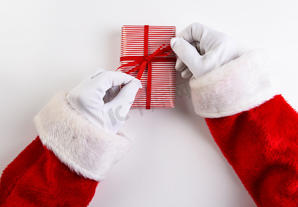 条纹丝带摄影照片_圣诞老人手在 res 和白色条纹圣诞礼物上绑丝带和蝴蝶结的高角度拍摄。