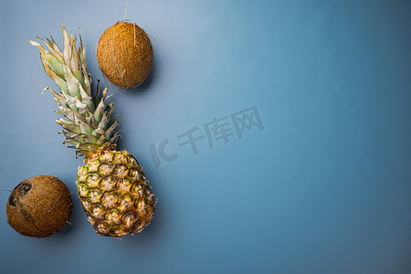 平铺菠萝摄影照片_新鲜的异国情调水果、菠萝和椰子，在蓝色质感的夏季背景中，顶视图平躺，带有文本复制空间