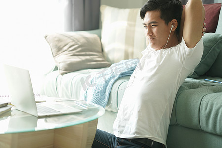 亚洲年轻学生男子企业家戴着耳机，在家里用电脑学习在线学习时，会感到疲倦、无聊、困倦。