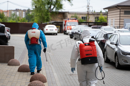 基辅摄影照片_乌克兰，基辅 - 2020 年 5 月 20 日：身穿白色防护服和面具的男子在冠状病毒流行期间对建筑物内表面进行消毒后走在街上。