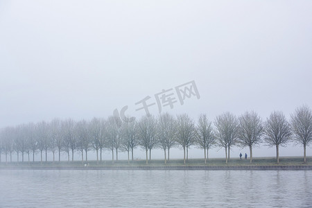 雾蒙蒙的早晨，两个人沿着荷兰树林间的运河漫步