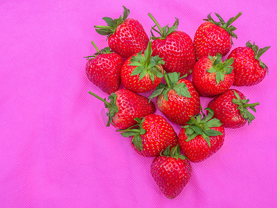 红色心形草莓甜果群，种子镶嵌在粉红色织物上的红色浆果心形水果的特写纹理