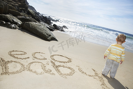 男孩 (1-2) 站在沙滩上写的 Eco Baby 文字旁