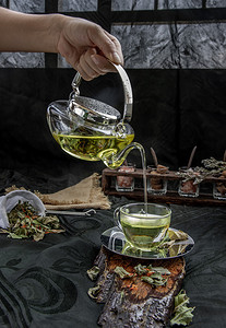 将带有印度沼泽飞蓬植物叶和红花干（藏红花替代品）的热香兰叶茶从玻璃茶壶中倒入装有茶草药和茶叶的玻璃杯中。