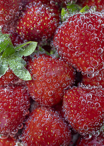 新鲜的红草莓和绿叶，在淡淡的苏打水中，上面布满了气泡。